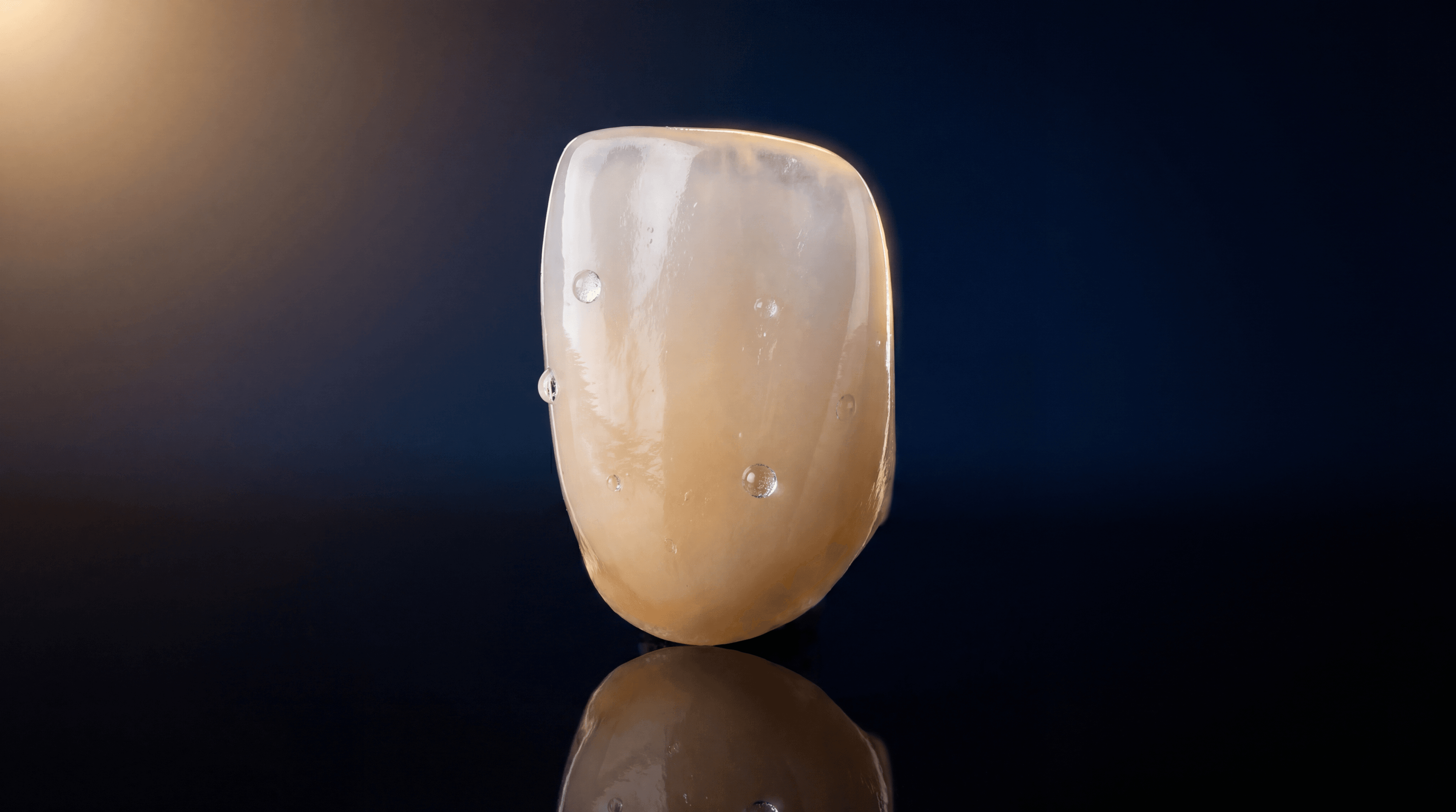 High-translucency monolithic zirconia anterior crown on pitch-black background with gold rim lighting